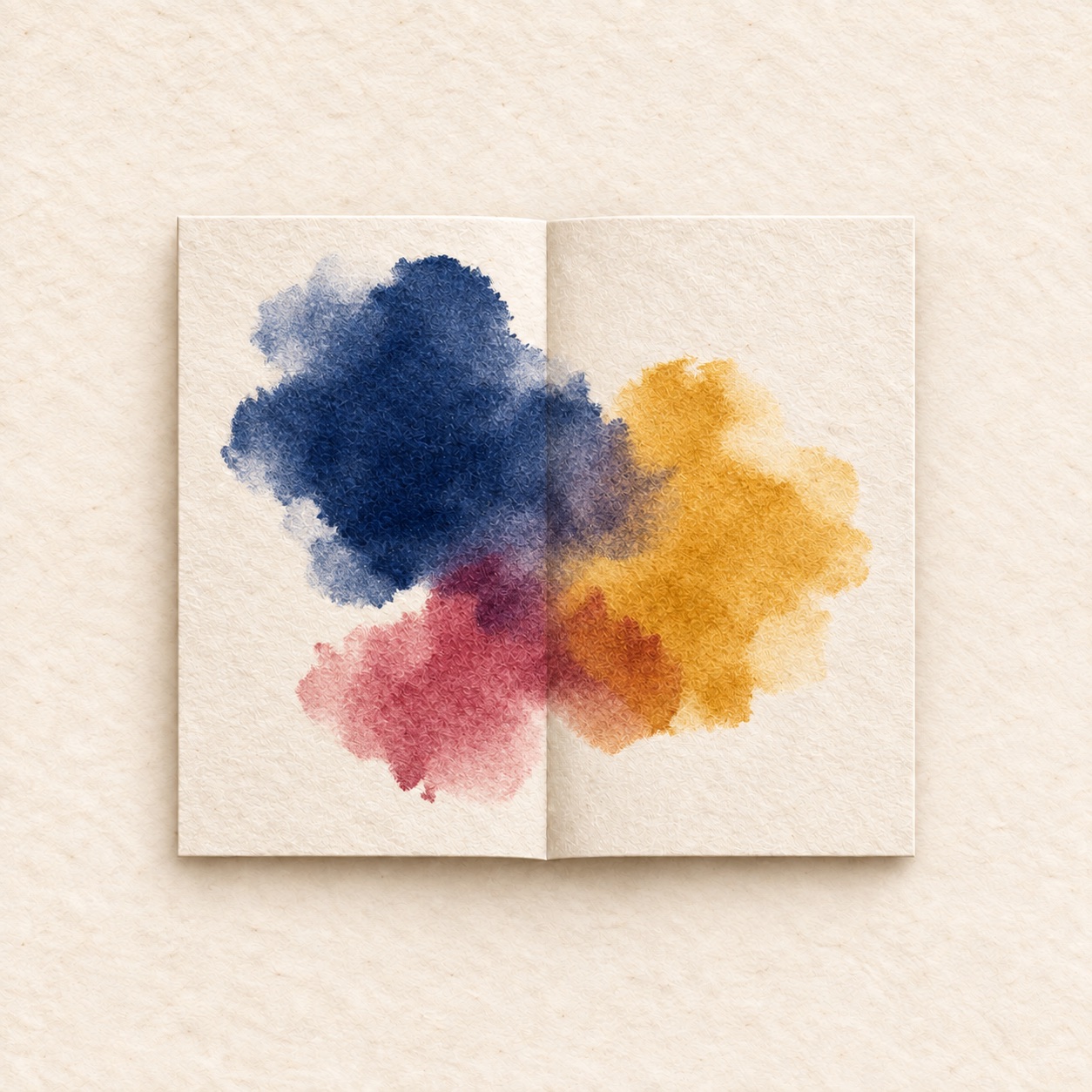 Indigo, mustard and rose ink softly overlapping across the centre crease of a textured paper sheet.